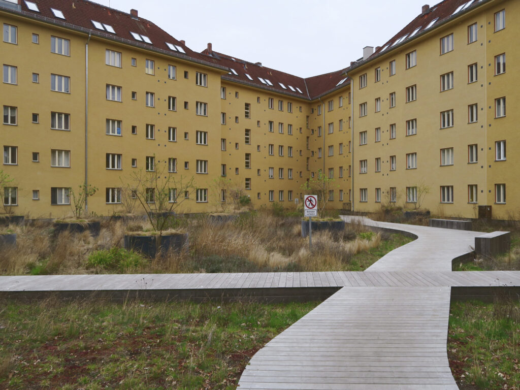 Blick in den gestalteten Innenhof und auf die ockerfarbenen Putzfassaden mit rot abgesetzten Details an den Fenstern.