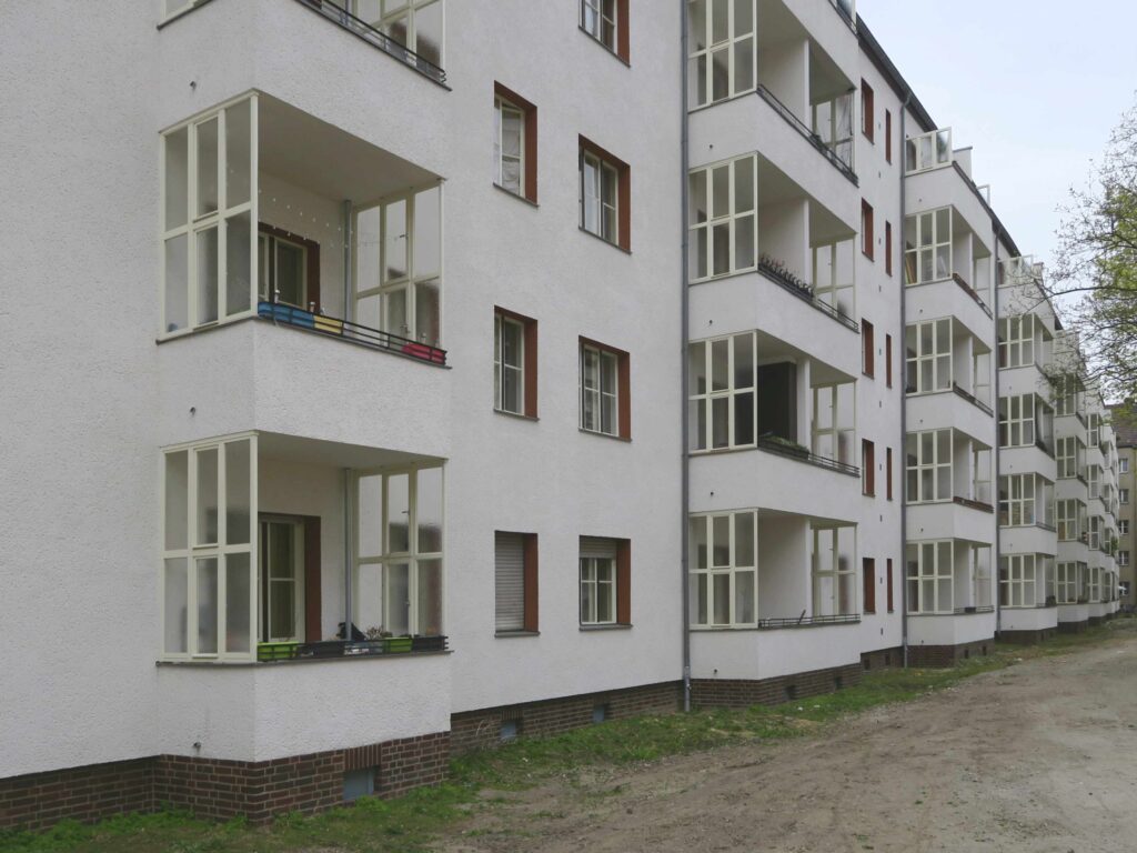 Blick auf die Fassade im Innenhof mit einer Reihe vorspringender Balkone und rot akzentuierten Fensterlaibungen.