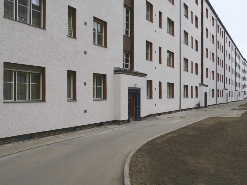 Blick auf die Fassade auf der Straßenseite mit den feingliedrig restaurierten Hauseingängen und den rot akzentuierten Fensterlaibungen.