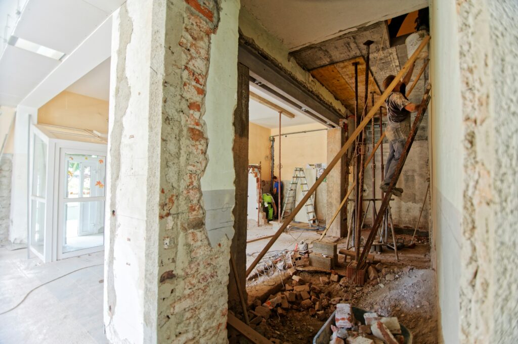 Blick in eine Sanierungsbaustelle. Ein Teil ist bereits abgerissen worden. Ein Handwerker steht auf einer Leiter.